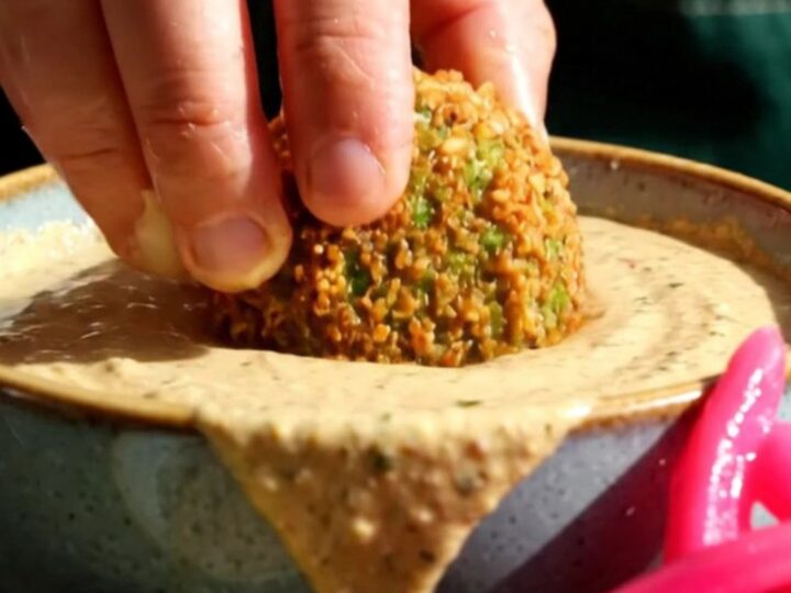 A close-up of a crispy, golden-brown falafel ball broken open to reveal a vibrant, emerald-green herb interior.