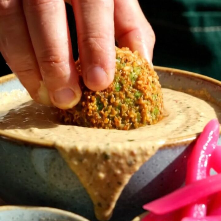 A close-up of a crispy, golden-brown falafel ball broken open to reveal a vibrant, emerald-green herb interior.