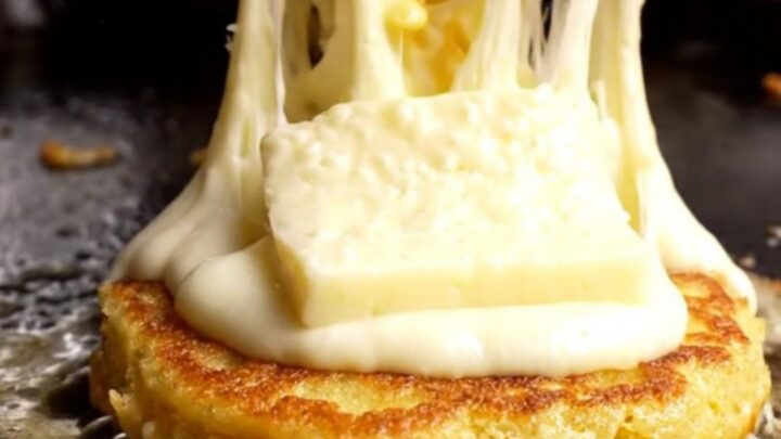 A golden, caramelized corn arepa split open to reveal a massive, dramatic stretch of melted white quesillo cheese.