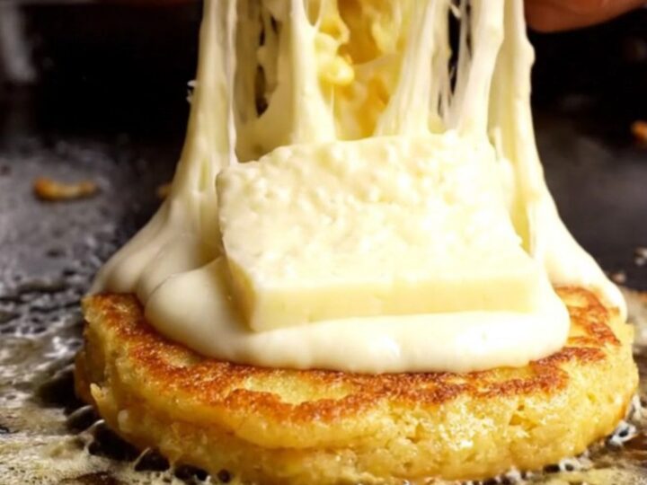 A golden, caramelized corn arepa split open to reveal a massive, dramatic stretch of melted white quesillo cheese.