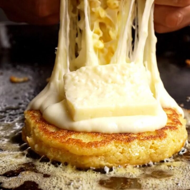 A golden, caramelized corn arepa split open to reveal a massive, dramatic stretch of melted white quesillo cheese.