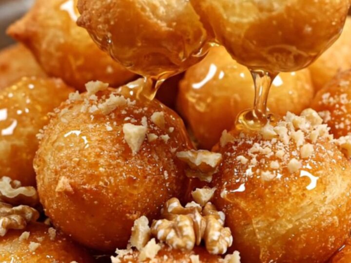 A close-up of golden, crispy Greek loukoumades drenched in shimmering thyme honey and topped with crushed walnuts.