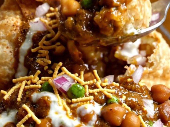 A clay bowl filled with smashed crispy samosas, spiced chickpeas, colorful chutneys, and fresh pomegranate seeds.
