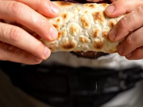 A crispy, freshly baked Turkish lahmacun topped with savory spiced lamb, rolled up and ready to eat.