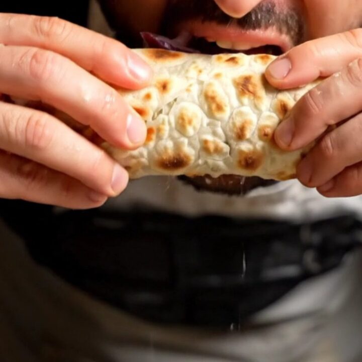 A crispy, freshly baked Turkish lahmacun topped with savory spiced lamb, rolled up and ready to eat.