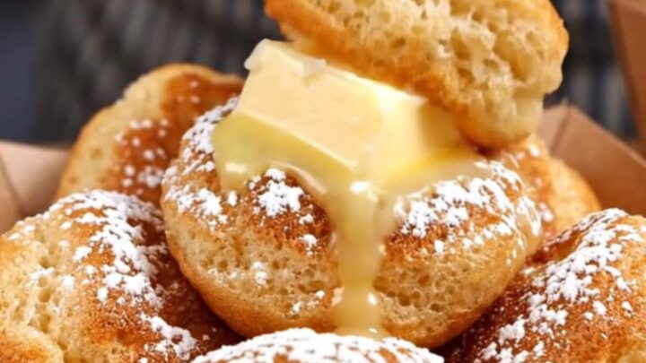 A close-up of golden, fluffy Dutch poffertjes in a dimpled cast-iron pan, topped with melting butter.