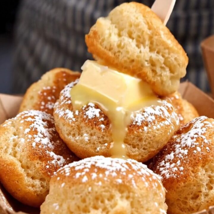 A close-up of golden, fluffy Dutch poffertjes in a dimpled cast-iron pan, topped with melting butter.