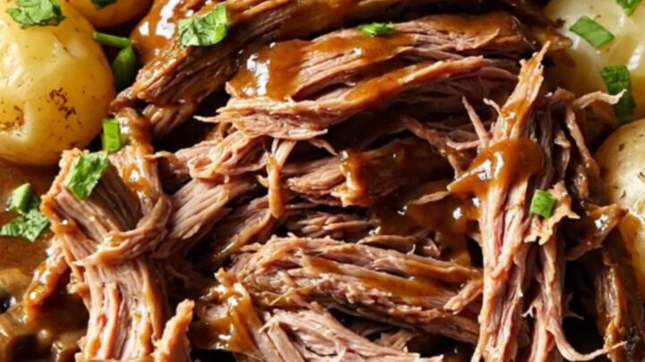 A close-up of a slow-cooked beef chuck roast in a gravy with potatoes, garnished with fresh green parsley.