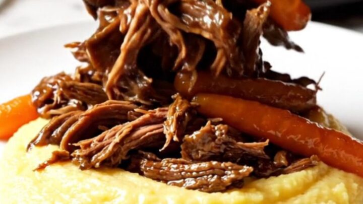 A close-up of a burgundy stoneware Crockpot showing shredded balsamic beef and glazed carrots.