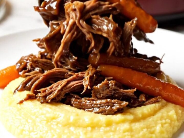 A close-up of a burgundy stoneware Crockpot showing shredded balsamic beef and glazed carrots.