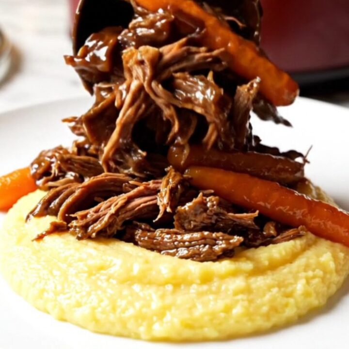 A close-up of a burgundy stoneware Crockpot showing shredded balsamic beef and glazed carrots.