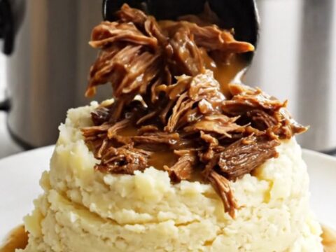 A close-up of shredded beef roast in a glossy brown gravy inside a white slow cooker.