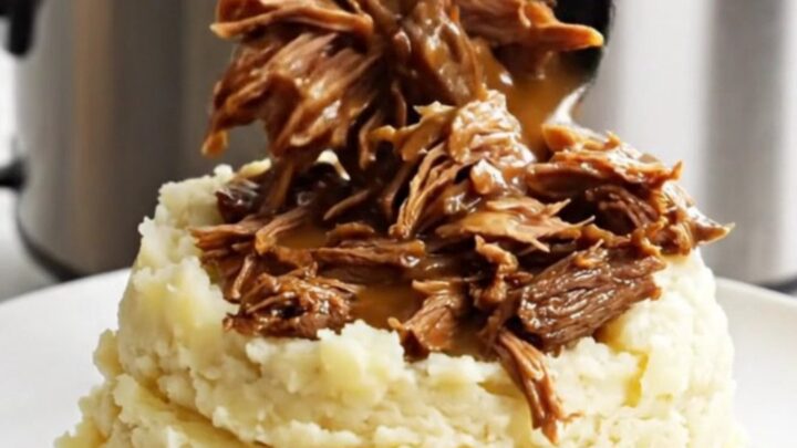 A close-up of shredded beef roast in a glossy brown gravy inside a white slow cooker.