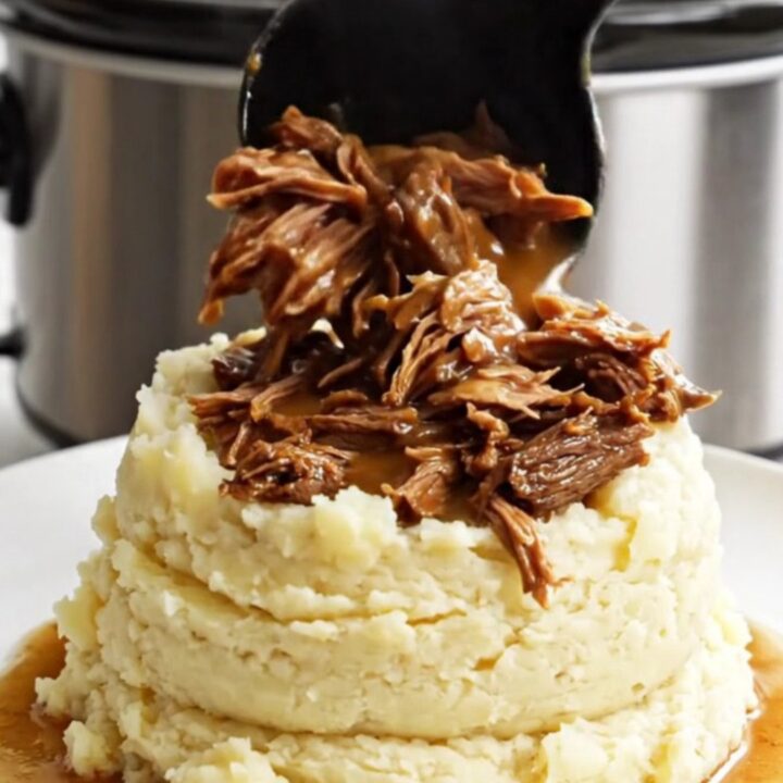 A close-up of shredded beef roast in a glossy brown gravy inside a white slow cooker.