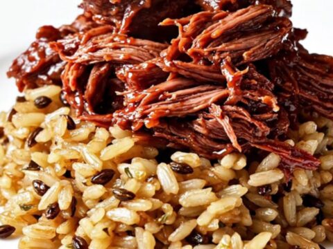 A ruby-red cranberry-orange braised beef roast served over wild rice with fresh rosemary garnishes.