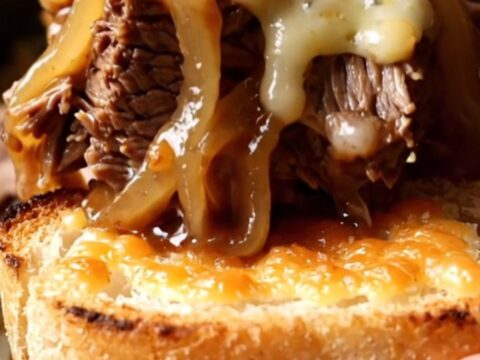 A close-up of a slow cooker filled with shredded beef chuck roast, caramelized onions, and melted Gruyère cheese.
