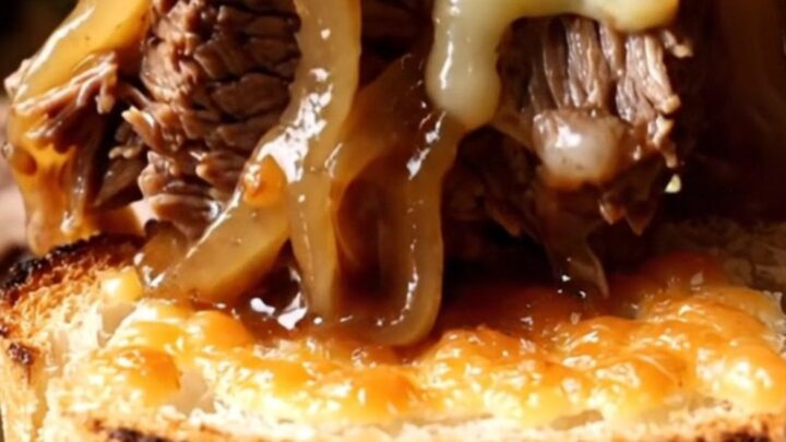 A close-up of a slow cooker filled with shredded beef chuck roast, caramelized onions, and melted Gruyère cheese.
