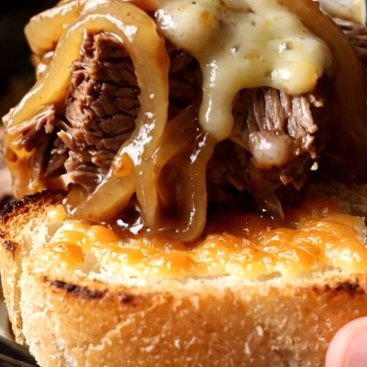 A close-up of a slow cooker filled with shredded beef chuck roast, caramelized onions, and melted Gruyère cheese.
