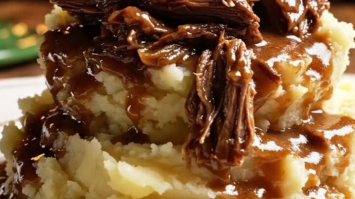 A close-up of a glossy dark green ceramic slow cooker filled with shredded stout-braised beef and pearl onions.