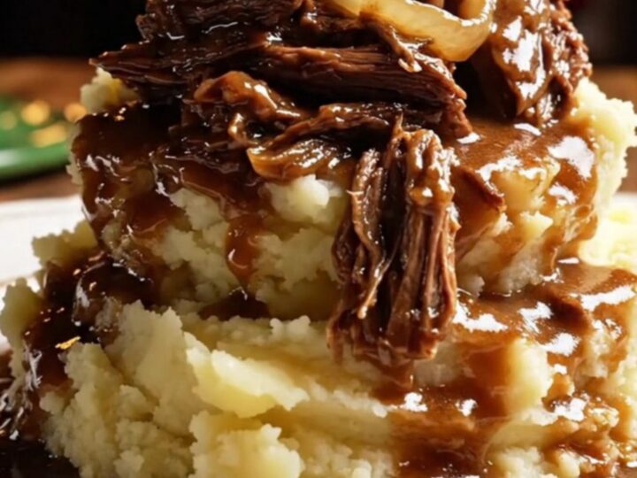 A close-up of a glossy dark green ceramic slow cooker filled with shredded stout-braised beef and pearl onions.