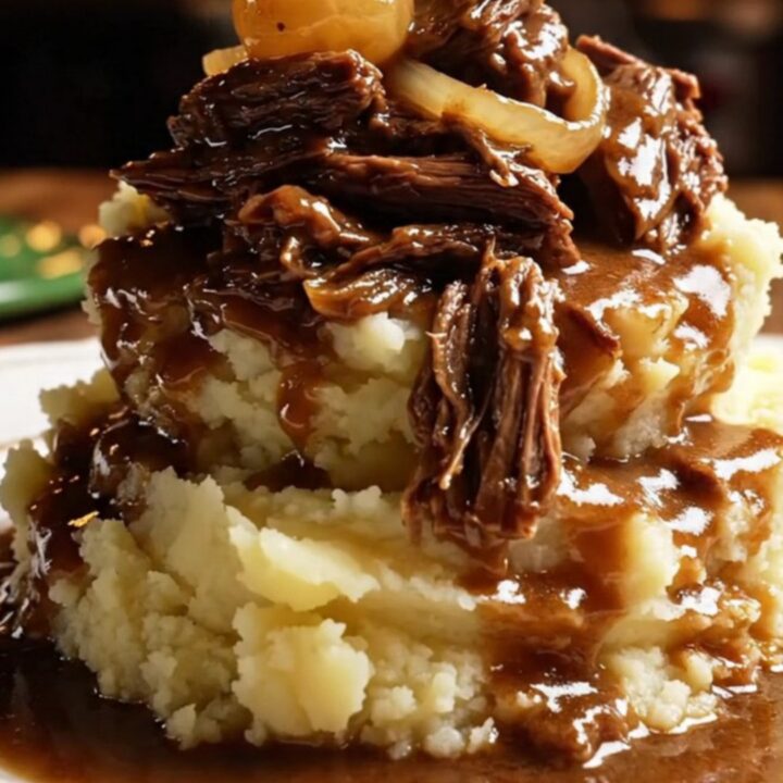 A close-up of a glossy dark green ceramic slow cooker filled with shredded stout-braised beef and pearl onions.