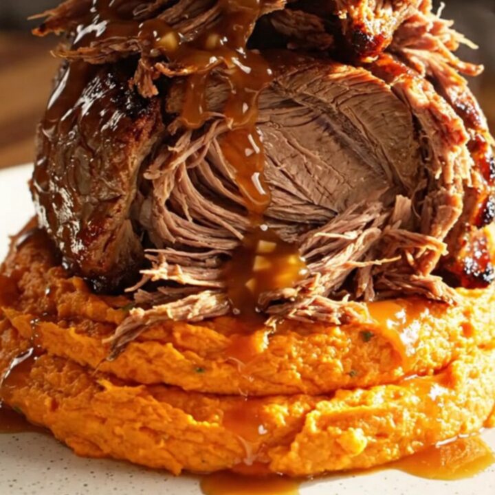 A close-up of a maple-bourbon Dijon shredded beef roast served in a rustic stoneware bowl.