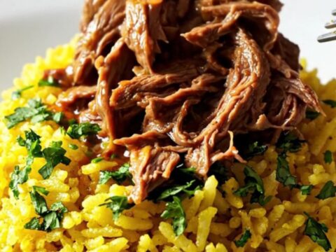 A close-up of a slow cooker filled with shredded beef, chorizo, and vibrant red sauce served over yellow rice.