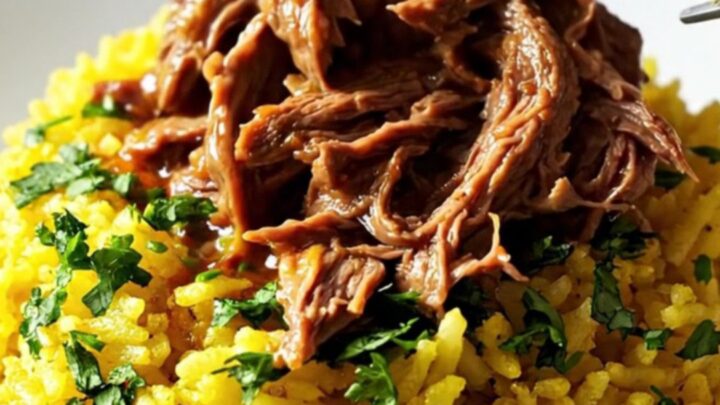 A close-up of a slow cooker filled with shredded beef, chorizo, and vibrant red sauce served over yellow rice.