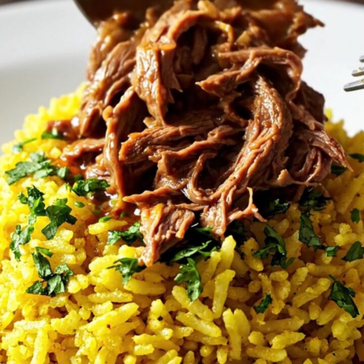 A close-up of a slow cooker filled with shredded beef, chorizo, and vibrant red sauce served over yellow rice.