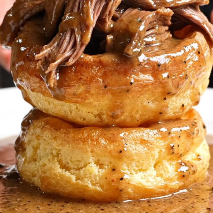 A close-up of a slow-cooked beef chuck roast being shredded with two forks