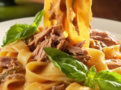 A close-up of a creamy Tuscan beef roast in a green ceramic slow cooker, topped with fresh basil.