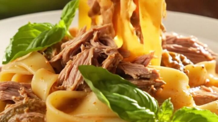 A close-up of a creamy Tuscan beef roast in a green ceramic slow cooker, topped with fresh basil.