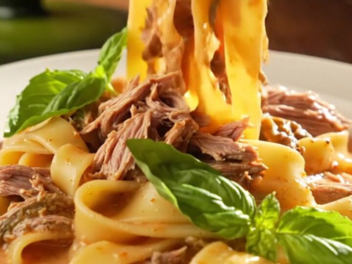A close-up of a creamy Tuscan beef roast in a green ceramic slow cooker, topped with fresh basil.