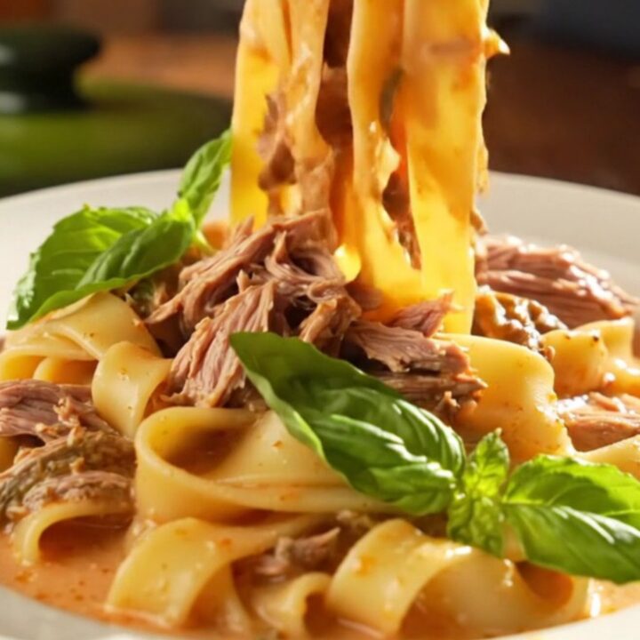 A close-up of a creamy Tuscan beef roast in a green ceramic slow cooker, topped with fresh basil.