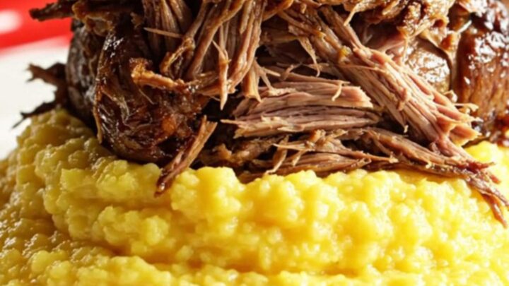Close-up of Coca-Cola braised beef being pulled apart by two forks, revealing tender fibers and caramelized Vidalia onions.
