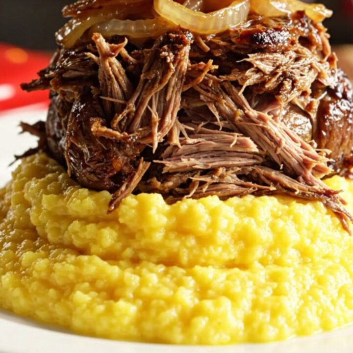 Close-up of Coca-Cola braised beef being pulled apart by two forks, revealing tender fibers and caramelized Vidalia onions.
