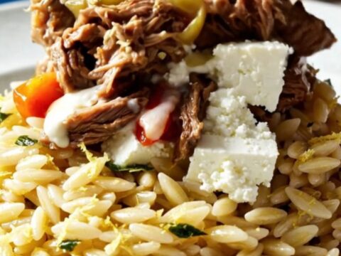 A close-up of Mediterranean shredded beef topped with crumbled feta, roasted red peppers, and olives.
