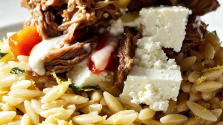 A close-up of Mediterranean shredded beef topped with crumbled feta, roasted red peppers, and olives.