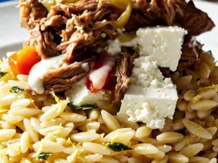 A close-up of Mediterranean shredded beef topped with crumbled feta, roasted red peppers, and olives.