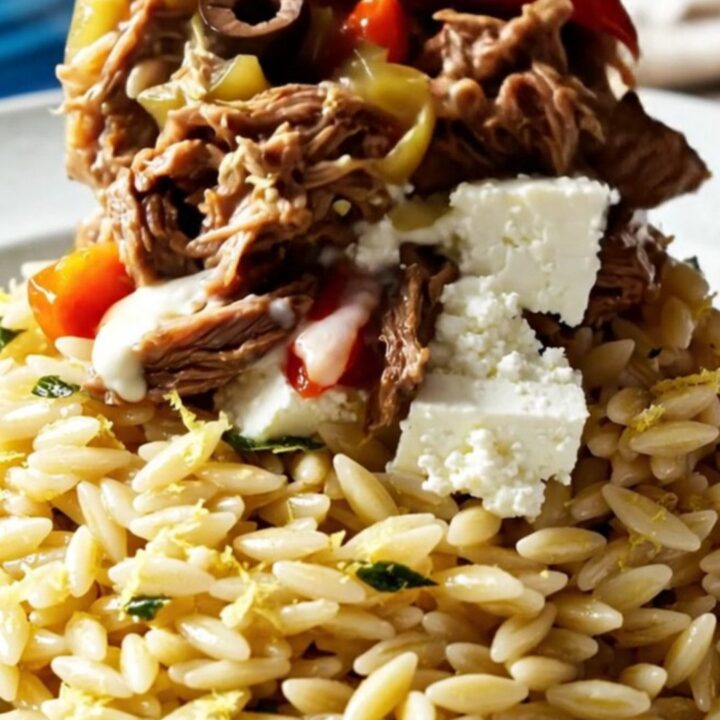 A close-up of Mediterranean shredded beef topped with crumbled feta, roasted red peppers, and olives.
