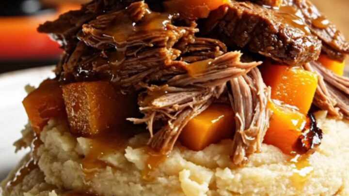 A close-up of shredded apple cider beef and tender butternut squash served over creamy mashed potatoes.