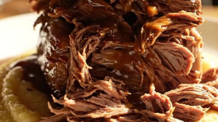 A close-up of a dark-crusted espresso chili-rubbed beef roast being shredded in a slow cooker.