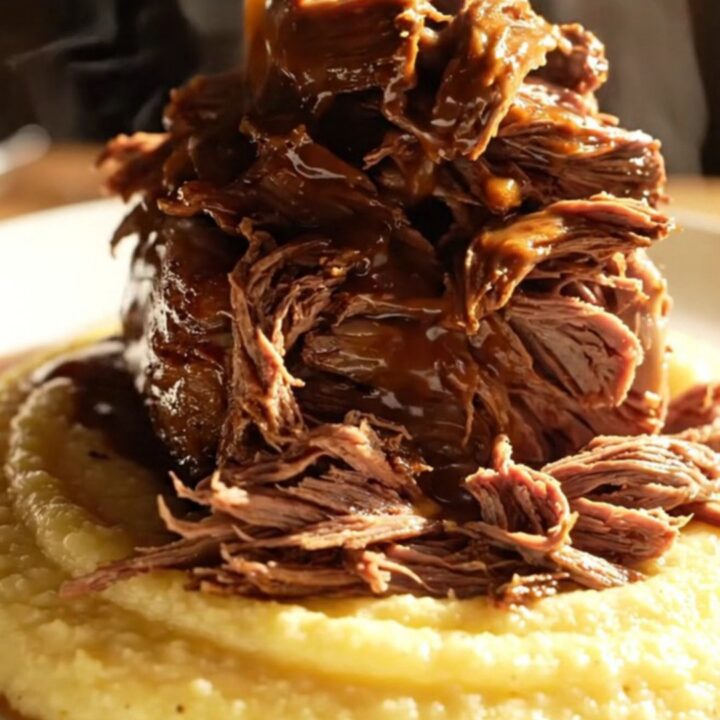 A close-up of a dark-crusted espresso chili-rubbed beef roast being shredded in a slow cooker.