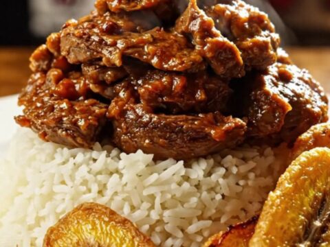 A close-up of tender, shredded Cuban Ropa Vieja served over white rice with fried plantains.