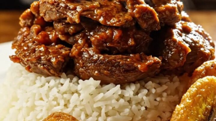A close-up of tender, shredded Cuban Ropa Vieja served over white rice with fried plantains.