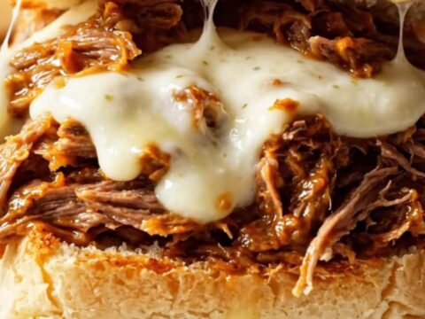 Close up of cheesy shredded beef sliders with melted mozzarella on Hawaiian rolls.