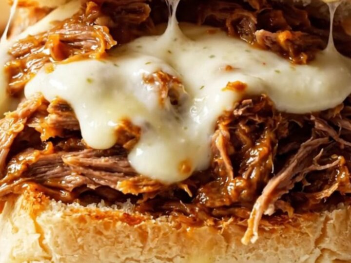 Close up of cheesy shredded beef sliders with melted mozzarella on Hawaiian rolls.