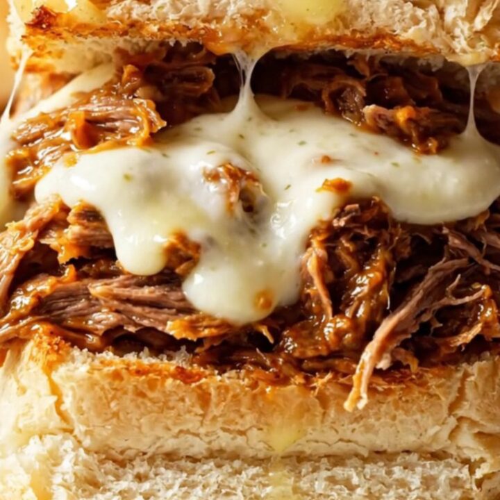Close up of cheesy shredded beef sliders with melted mozzarella on Hawaiian rolls.