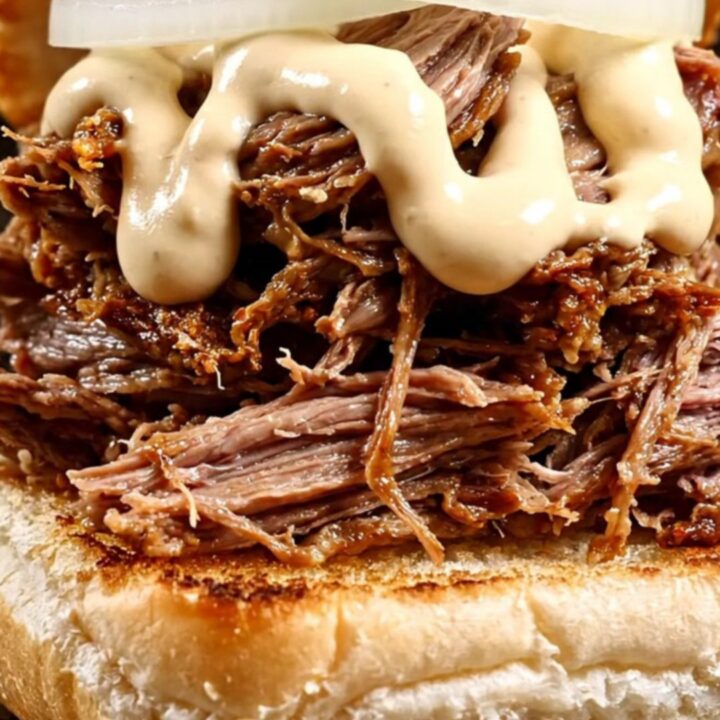 A close-up of a smoky shredded beef sandwich on a toasted kaiser roll with horseradish sauce.