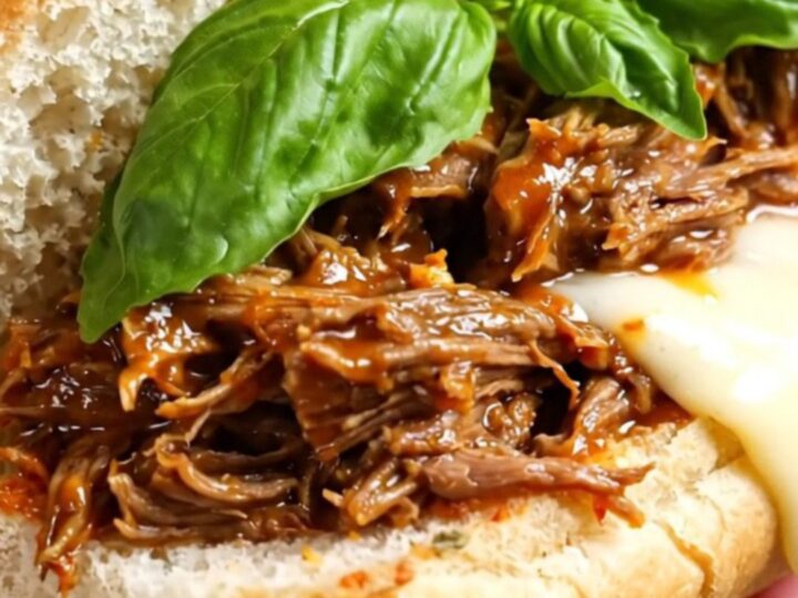 A close-up of a cheesy, pepperoni-topped shredded beef sub sandwich on a wooden board.